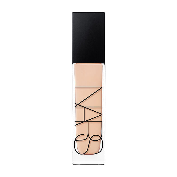 Woman applying NARS foundation with fingertips, blending from centre of face outward